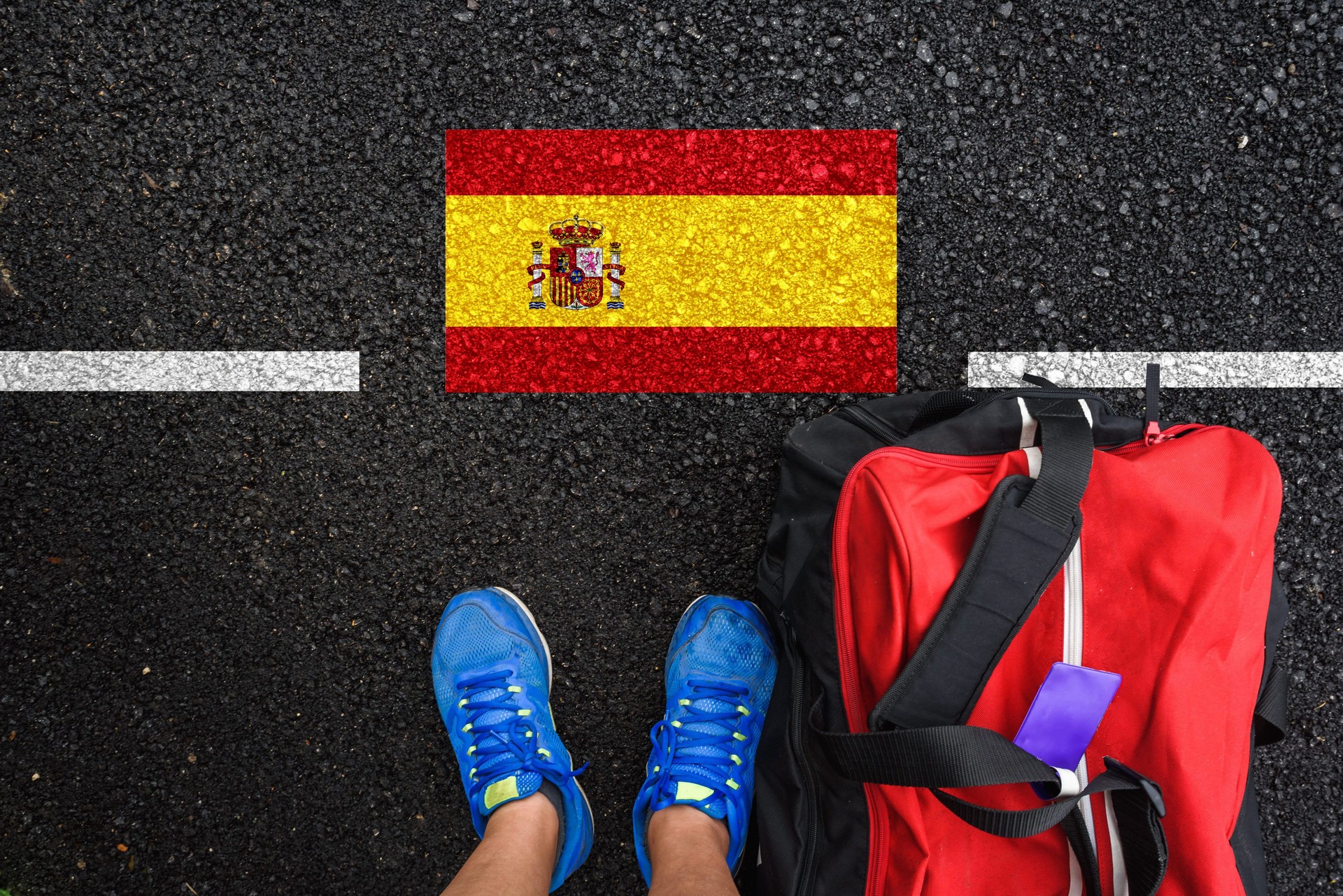a man with a shoes and travel bag is standing on asphalt next to flag of Spain and border a man with a shoes and travel bag is standing on asphalt next to flag of Spain and border